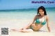 A woman in a blue bikini sitting on the beach.