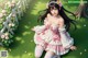 A girl in a pink and white dress sitting on the grass.